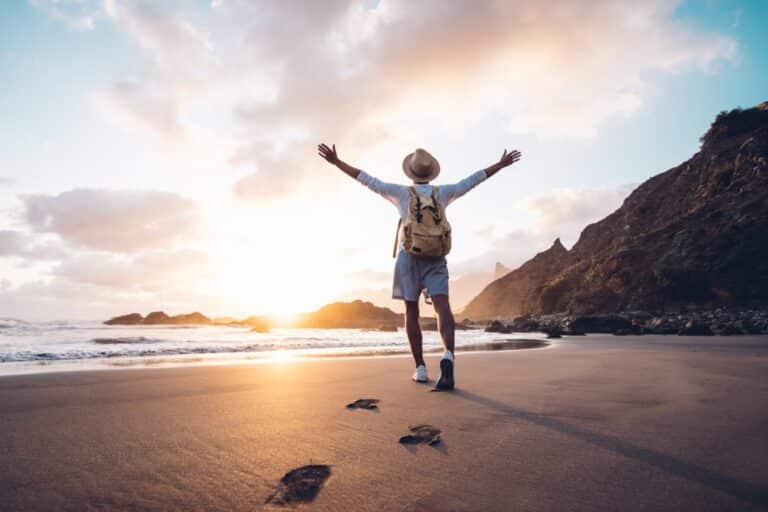 Young man at the beach with arms outstretched enjoying the sunrise