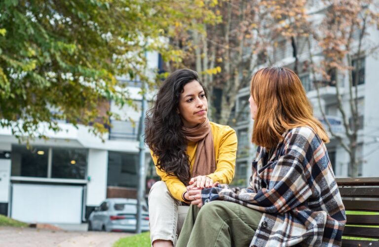 Young women sitting on a bench as one friend helps the other